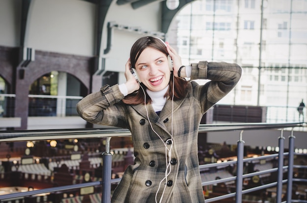 Cheerful happy brunette slender girl in a shopping center having fun listening to music in headphones