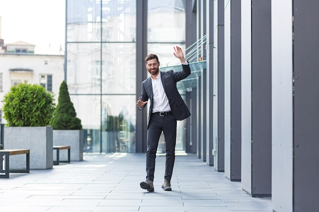 Cheerful happy business man dancing walk the city street background a modern office building outside, outdoors Funny successful businessman in suit celebtes victory