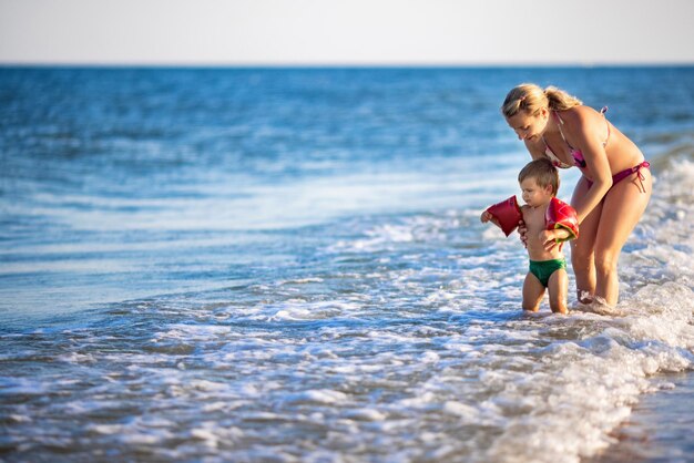 Cheerful happy caring mom throws her little funny son up over the calm blue sea on a warm summer sunny vacation under the warm sun