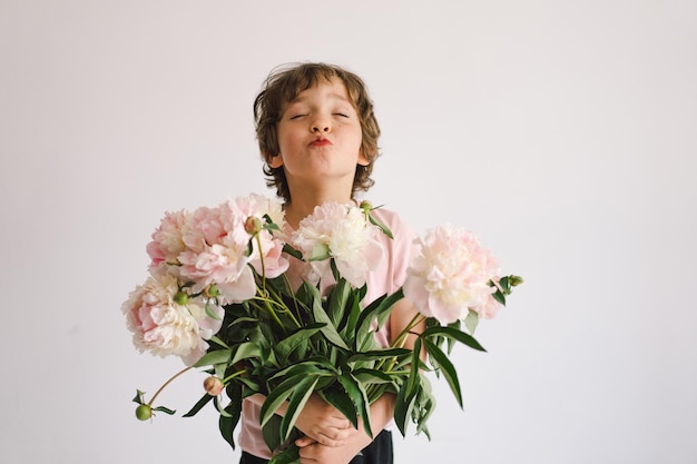 Cheerful happy child with Peonys bouquet Smiling little boy on white background Mother's Day Love and romantic concept