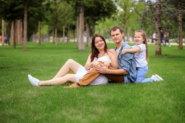 Cheerful happy family embracing and looking at camera while resting on green grass on sunny day in park