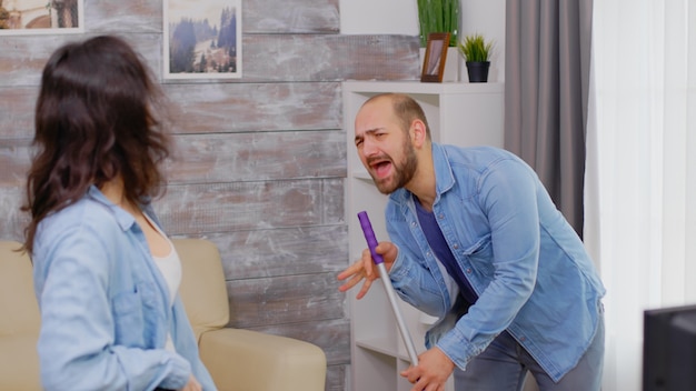 Cheerful husband and wife singing while cleaning the house