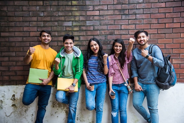 Cheerful Indian asian young group of college students or friends laughing together while sitting, standing or walking in campus