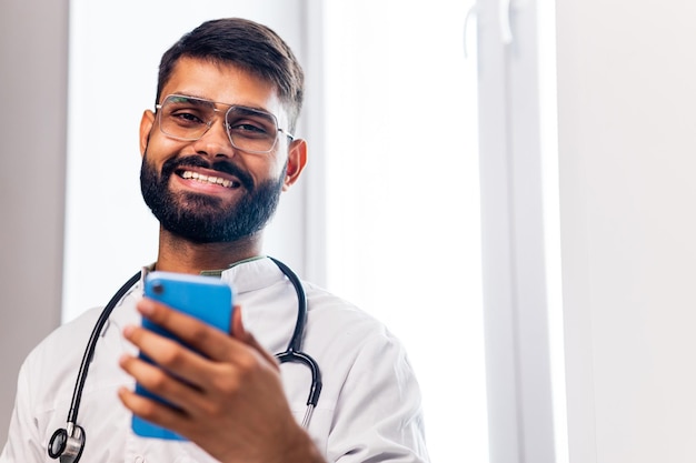 Cheerful indian doctor using application on mobile phone in hospital