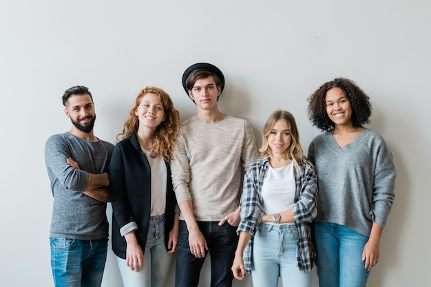 Cheerful intercultural friends in stylish casualwear looking at you while standing against white wall in studio