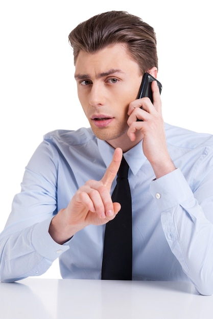 Cheerful interviewer. Handsome young man in shirt and tie sitting at the table and gesturing while isolated on white