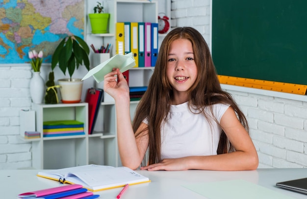 Cheerful kid girl hold paper plane at school lesson school