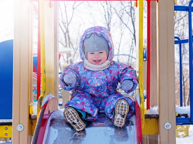 Cheerful kid rides down slide in sunny frosty day in winter, Children Protection Day