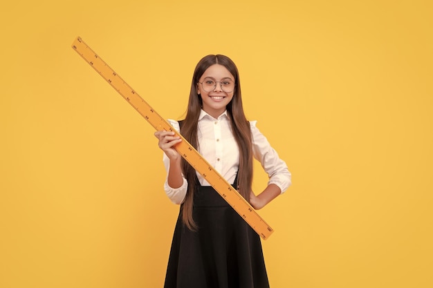 Cheerful kid in school uniform and glasses hold mathematics ruler for measuring geometry