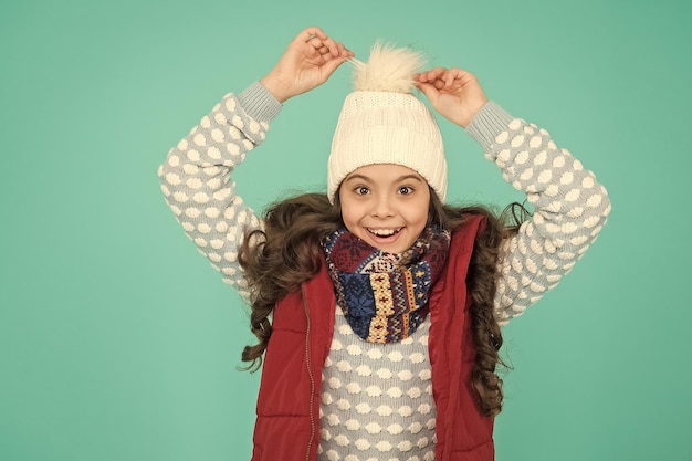 Cheerful kid in warm winter clothing of knitted hat scarf and sweater on new year holidays happy childhood