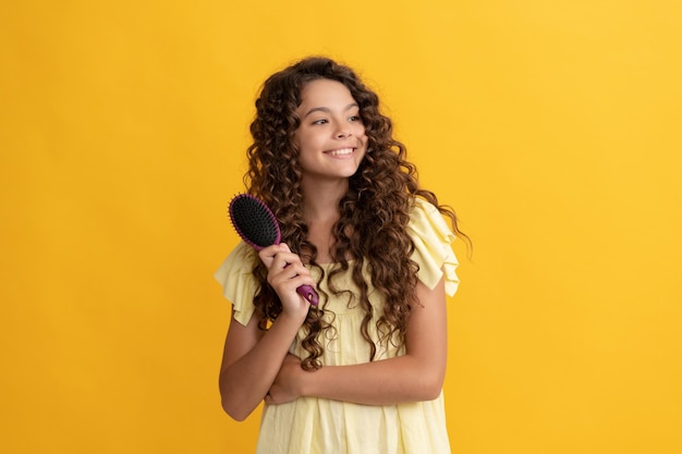 Cheerful kid with curly hair hold hairbrush teen beauty hairstyle fashion model combing frizzy curl girl has wavy hairdo portrait of frizz child haircare and hair loss hairdresser