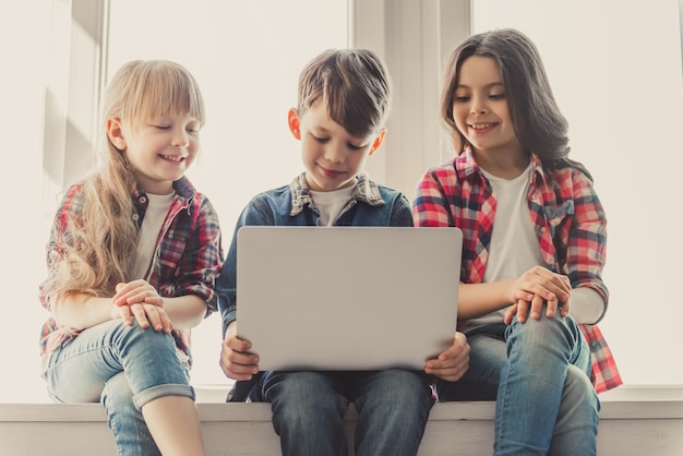 Cheerful kids in casual clothes are using a laptop.