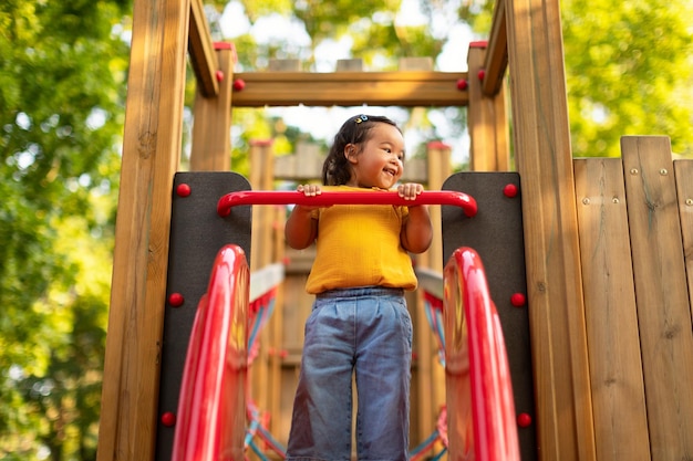 Cheerful korean baby girl standing on slide at outdoor playground