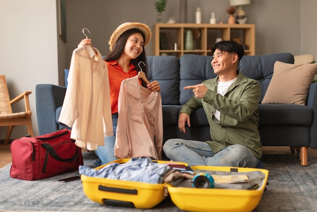 Cheerful korean travelers spouses packing travel suitcase choosing clothes indoors