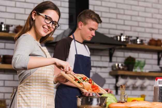 Cheerful lady cooking salad near boyfriend