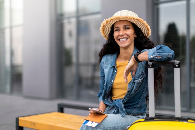 Cheerful lady tourist sitting on bench outside airport copy space