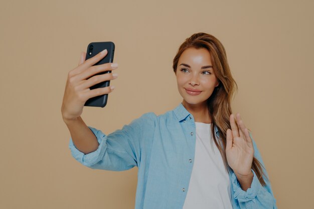 Cheerful lady waving at camera on beige background