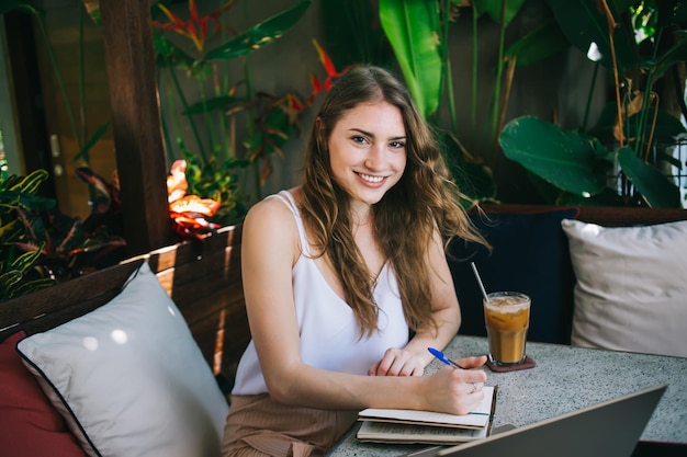 Cheerful lady writing in notebook while sitting near plants