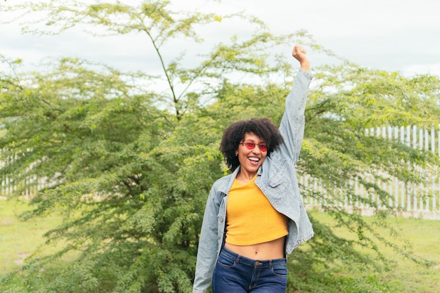 Cheerful Latin Afro woman posing outdoors with green plants in the background