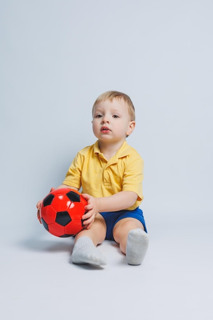 Cheerful little boy 56 years old football fan in a yellow Tshirt supports the team holds a soccer ball in his hands isolated on a white background The concept of sports family recreation