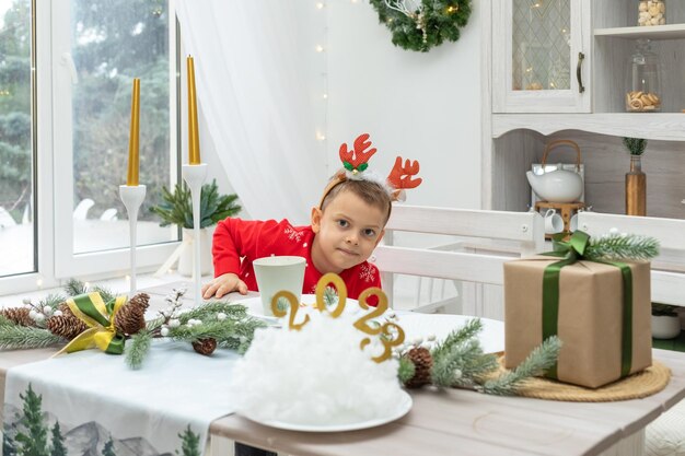 Cheerful little boy wearing red sweater deer horns on head eat dry orange slices