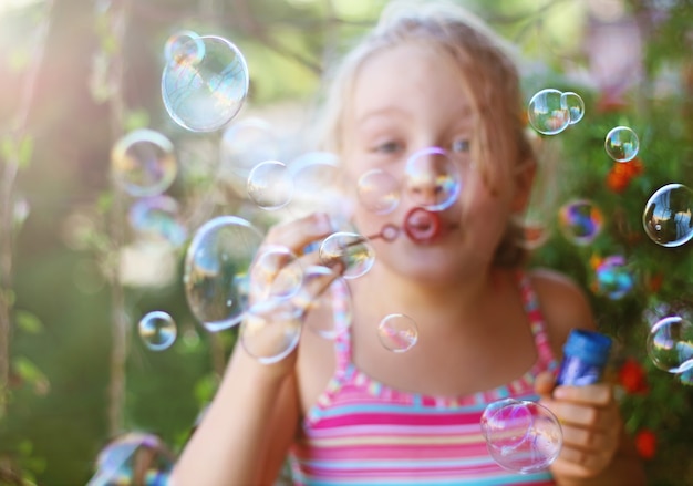 Cheerful little girl blows soap bubbles outdoor in summer