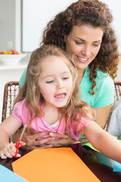 Cheerful little girl doing arts and crafts with mother at the table at home in kitchen