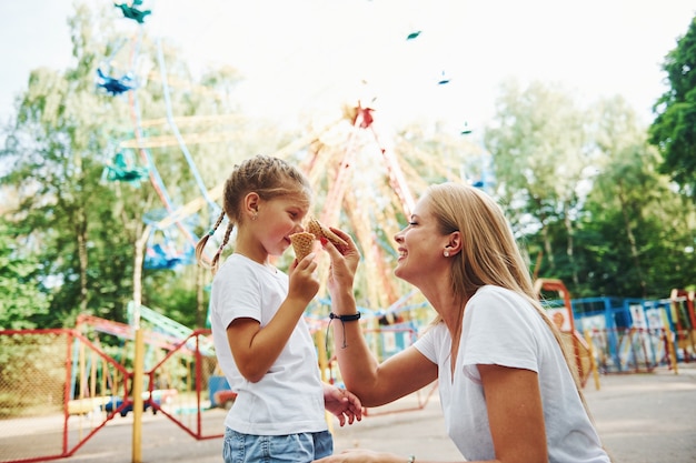 Cheerful little girl her mother have a good time in the park together near attractions