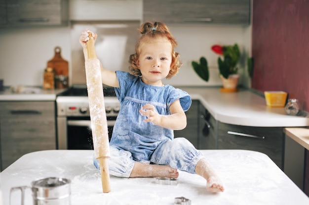 Cheerful little girl, soiled in flour, sitting on the table