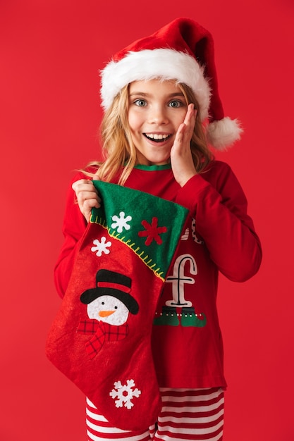 Cheerful little girl wearing Christmas costume standing isolated, taking presents from a Christmas sock