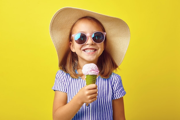 Cheerful little girl with ice cream on yellow isolated background