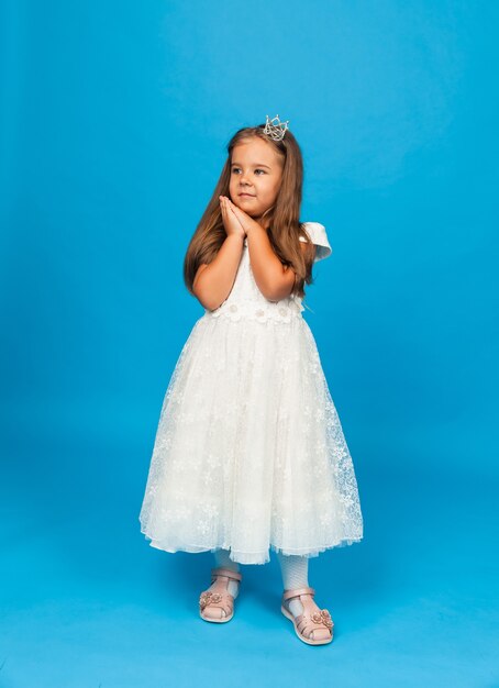 Cheerful little girl with long hair in a princess dress and with a crown.