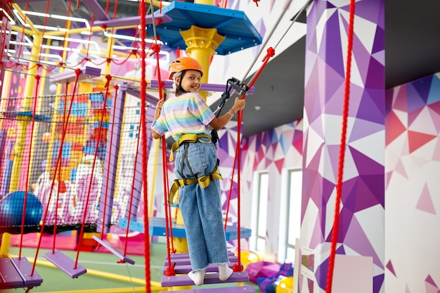 Cheerful little girl on zip line in entertainment center. Children having fun in climbing area, kids spend the weekend on playground, happy childhood