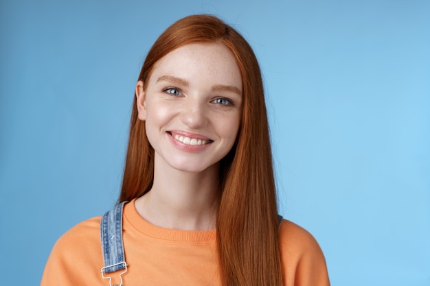 Cheerful lively redhead caucasian girl smiling happily look camera kind sincere friendly talking have perfect summer holidays talking friends standing blue background joyful