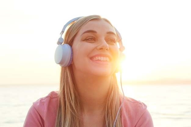 Cheerful lovely woman in sunset light glare on her face enjoying music in headphones