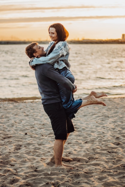 Cheerful lovers hug on the beach. A romantic date in the sunset.