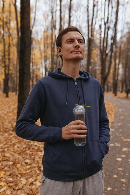 Cheerful male athlete with reusable bottle of water standing in park and having break