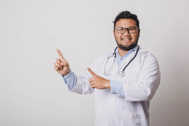 Cheerful male doctor with sideways pointing gesture at copy space isolated on white background