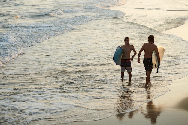 Cheerful male friends surfing in ocean before sunset