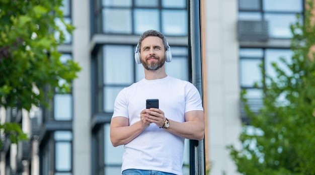 Cheerful man choosing music playlist outside photo of man choose music playlist on phone