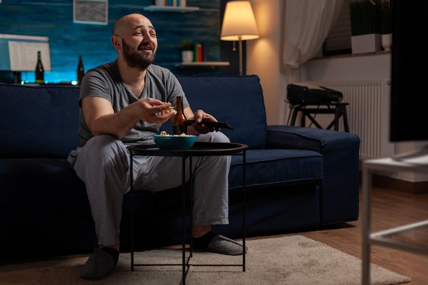 Cheerful man eating popcorn and laughing at comedy film on television channel, having fun with entertainment activity. Person feeling happy about watching funny movie, in leisure time.