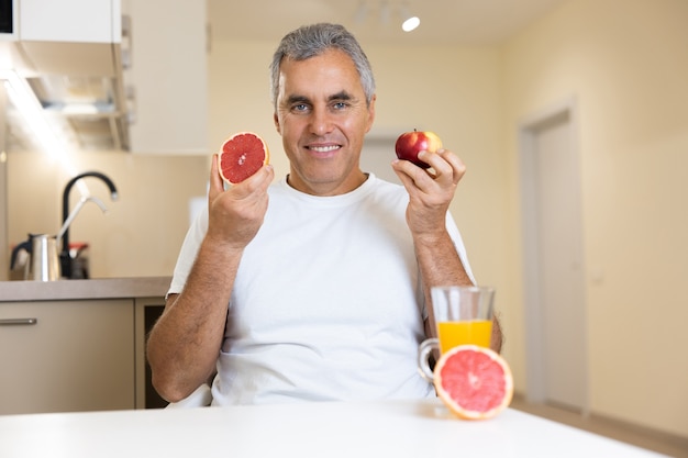 Cheerful man holding apple and grapefruit near face and smiling