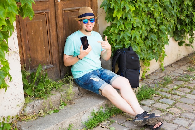 Cheerful man holding and pointing smartphone outdoor.