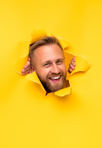 Cheerful man looking through torn paper