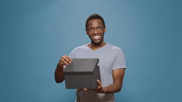 Cheerful man opening present box to see purchase on camera, unpacking cardboard shopping order. Person smiling and unboxing delivery package shipment from ecommerce retail store.