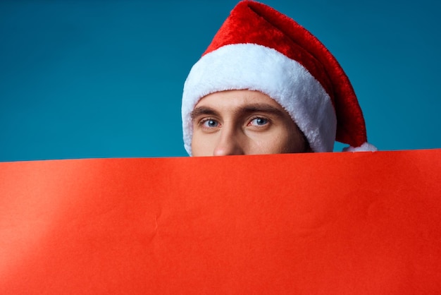 Cheerful man in a santa hat holding a banner holiday blue background