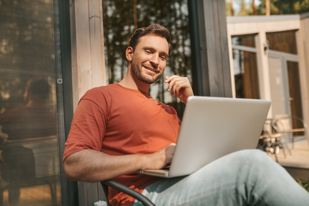 Cheerful man sitting with laptop outdoors