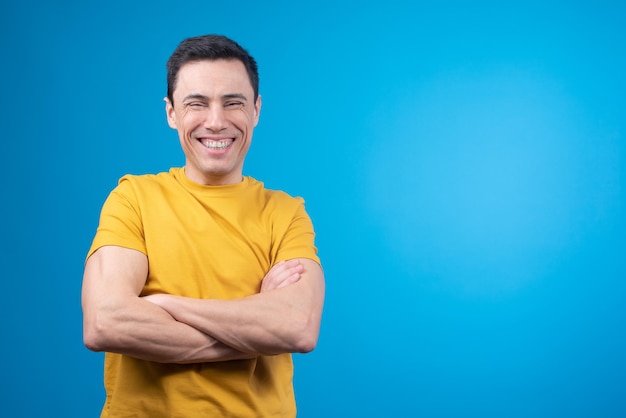 Cheerful man standing with crossed arms and laughing in studio