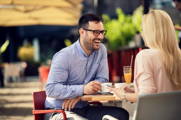 Cheerful man talking to his girlfriend who is using mobile phone in a cafe