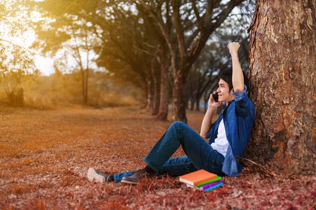 cheerful man talking on mobile phone with hand raised in park